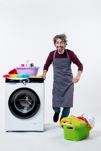 Vorderansicht glücklicher Haushältermann, der in der Nähe einer weißen Waschmaschine auf weißem Hintergrund steht