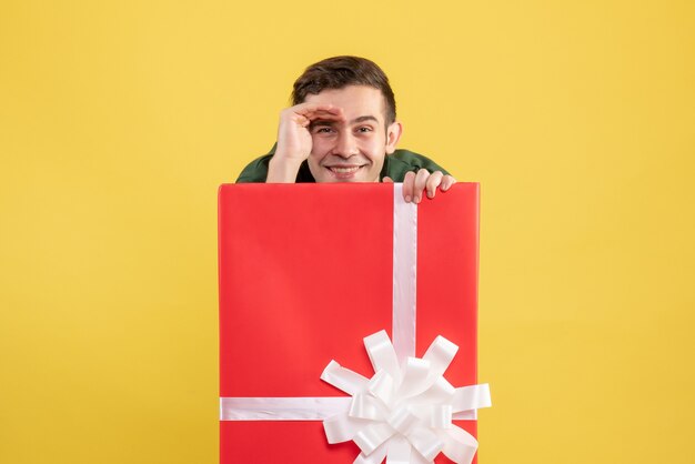 Vorderansicht glücklicher junger Mann, der hinter großer Geschenkbox auf Gelb steht