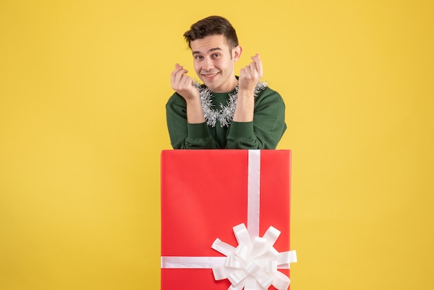 Vorderansicht glücklicher junger Mann, der hinter großer Geschenkbox auf Gelb steht