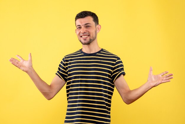 Vorderansicht glücklicher junger Mann im schwarz-weiß gestreiften T-Shirt, das Hände auf gelbem lokalisiertem Hintergrund öffnet