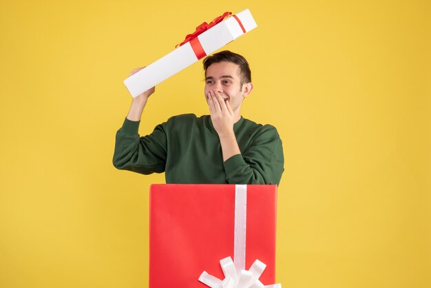 Vorderansicht glücklicher junger Mann mit Kastenabdeckung, die hinter großer Geschenkbox auf Gelb steht