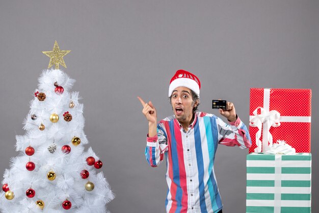 Vorderansicht glücklicher junger Mann Point Finger zeigt weißen Weihnachtsbaum