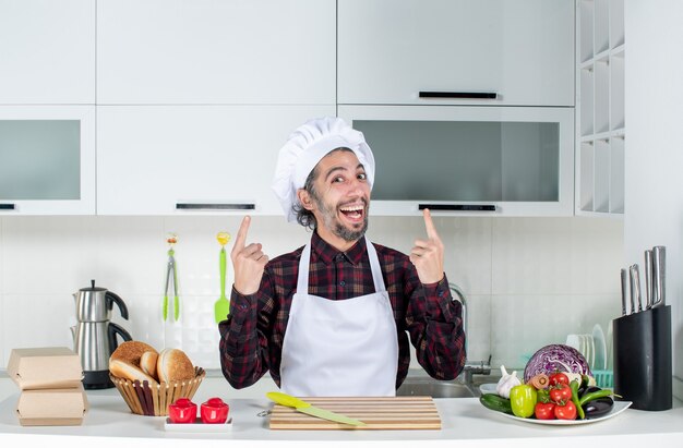 Vorderansicht glücklicher Mann, der hinter Küchentisch in der Küche steht