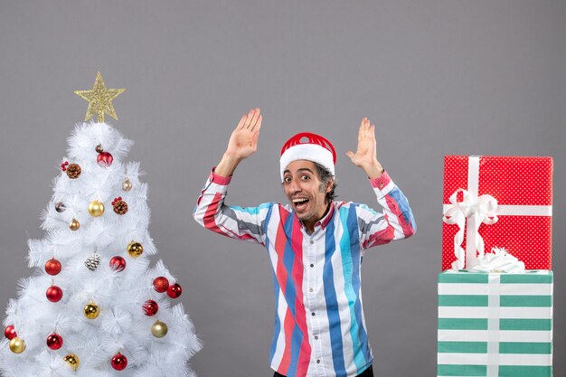 Vorderansicht glücklicher Mann, der seine Hände nahe weißem Weihnachtsbaum aufstellt