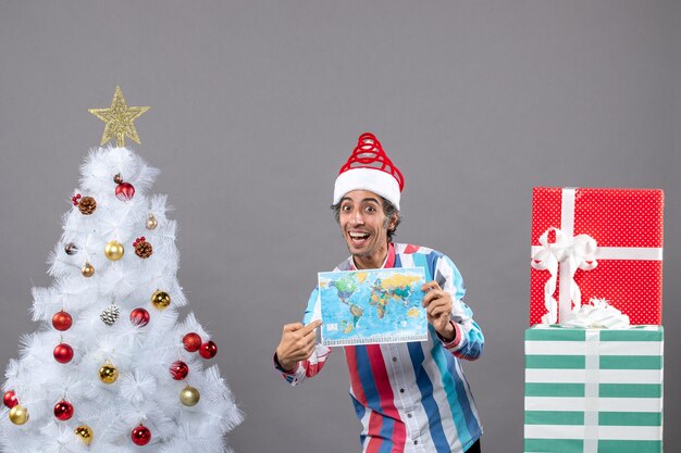 Vorderansicht glücklicher Mann mit Spiralfeder-Weihnachtsmütze, die auf Weltkarte zeigt