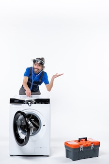 Vorderansicht glücklicher mechaniker mit stirnlampe, der das stethoskop auf die waschmaschine auf den weißen raum legt Kostenlose Fotos