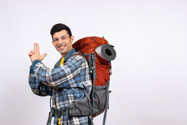 Vorderansicht glücklicher reisender Mann mit Rucksack, der Fingerpistole macht