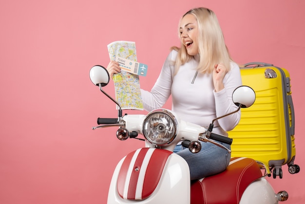 Vorderansicht glückliches blondes Mädchen auf Moped, das Ticket und Karte hält
