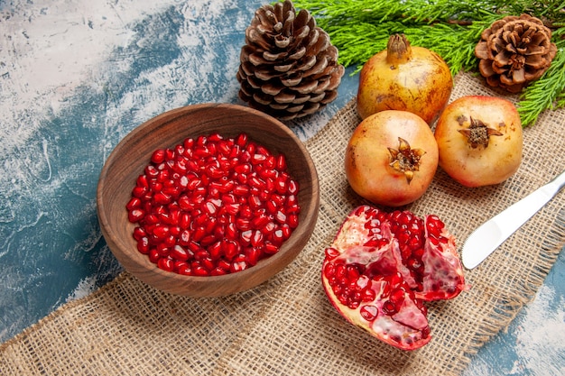 Vorderansicht Granatapfelkerne in Holzschale Abendessen Messer Granatäpfel Tannenzweig auf blau-weißem Hintergrund