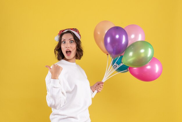 Vorderansicht hübsche Frau, die bunte Luftballons auf Gelb hält