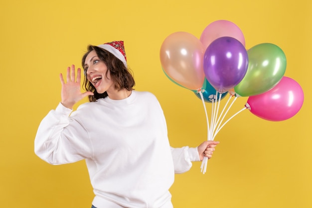 Vorderansicht hübsche Frau, die bunte Luftballons auf Gelb hält