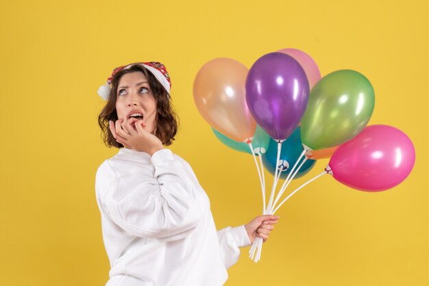 Vorderansicht hübsche Frau, die bunte Luftballons auf Gelb hält