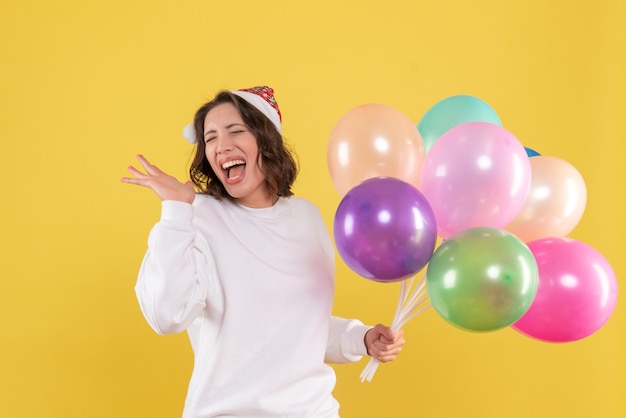 Vorderansicht hübsche Frau, die bunte Luftballons auf Gelb hält