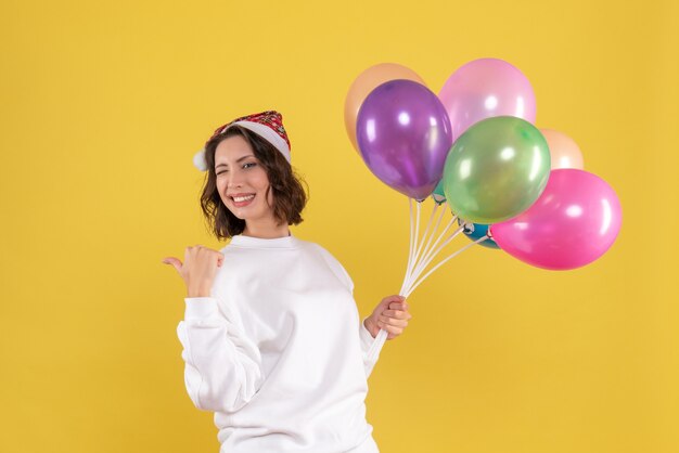 Vorderansicht hübsche Frau, die bunte Luftballons auf Gelb hält