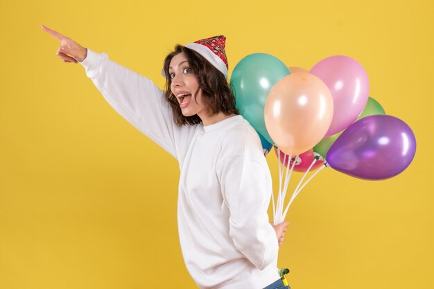 Vorderansicht hübsche Frau, die bunte Luftballons auf Gelb versteckt