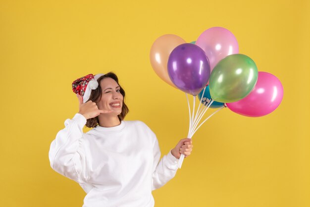 Vorderansicht hübsche Frau, die bunte Luftballons auf gelbem Schreibtisch Neujahrsgefühlsfrauenfarbweihnachten hält