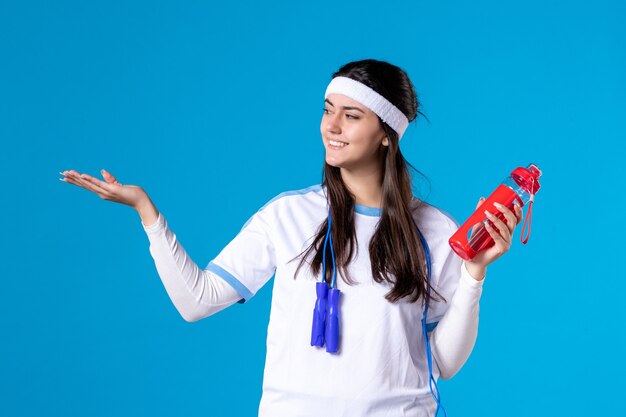 Vorderansicht hübsche Frau in Sportkleidung mit Flasche Wasser auf Blau