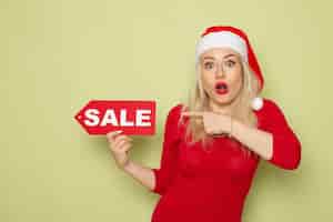 Kostenloses Foto vorderansicht hübsche weibliche holdingverkaufsschrift auf grüner wandschnee-emotion-weihnachtsneujahrsfarbe