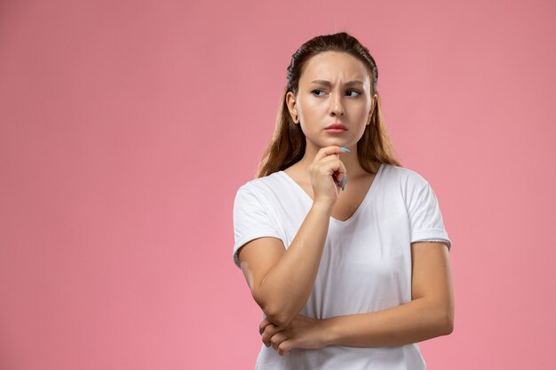 Vorderansicht junge attraktive Frau im weißen T-Shirt, das auf dem rosa Hintergrund aufwirft und denkt