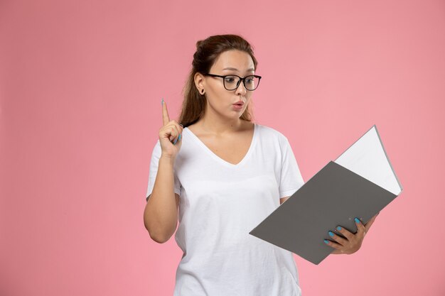 Vorderansicht junge attraktive Frau im weißen T-Shirt, das graue Datei auf rosa Hintergrund liest