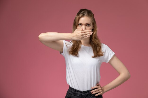 Vorderansicht junge attraktive Frau im weißen T-Shirt, das ihren Mund auf dem dunkelrosa Wandmodellfarbe weibliches junges Mädchen bedeckt