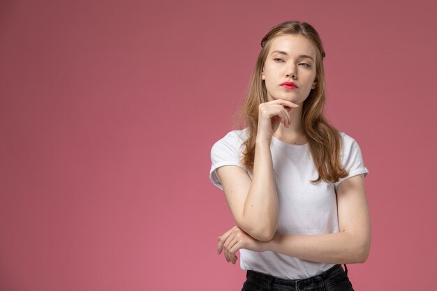 Vorderansicht junge attraktive Frau im weißen T-Shirt, das mit denkendem Ausdruck auf dem weiblichen jungen Mädchen der rosa Wandmodellfarbe aufwirft