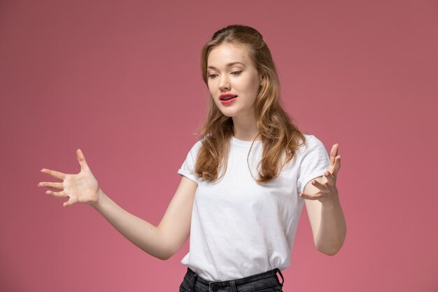 Vorderansicht junge attraktive Frau im weißen T-Shirt, das mit emotionaler Weise auf rosa Wandmodell weibliches Posefarbfoto aufwirft