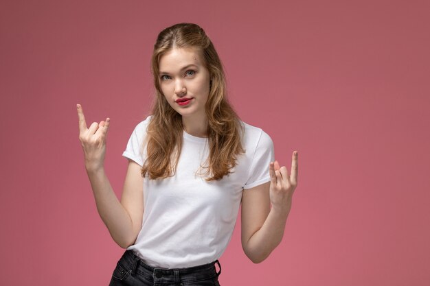 Vorderansicht junge attraktive Frau im weißen T-Shirt, das mit Rocker-Pose auf weiblichem Pose-Farbfoto des rosa Wandmodells aufwirft