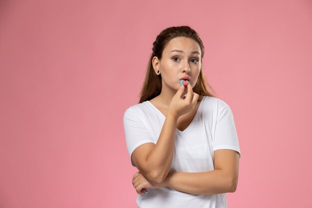 Vorderansicht junge attraktive Frau im weißen T-Shirt gerade posierend, die ihre Lippen auf dem rosa Hintergrund berührt