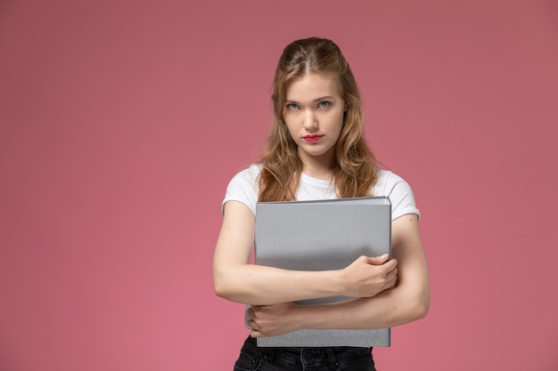 Vorderansicht junge attraktive Frau im weißen T-Shirt posiert mit grauem Dokument auf rosa Schreibtischmodell weiblich Pose Farbfoto Jugend weiblich