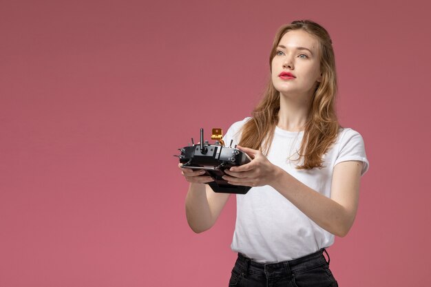 Vorderansicht junge attraktive Frau im weißen T-Shirt posiert und hält Fernbedienung auf rosa Wandmodell weiblich Pose Farbfoto weiblich jung