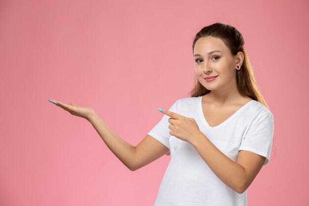 Vorderansicht junge attraktive Frau im weißen T-Shirt smi, das auf dem rosa Hintergrund aufwirft