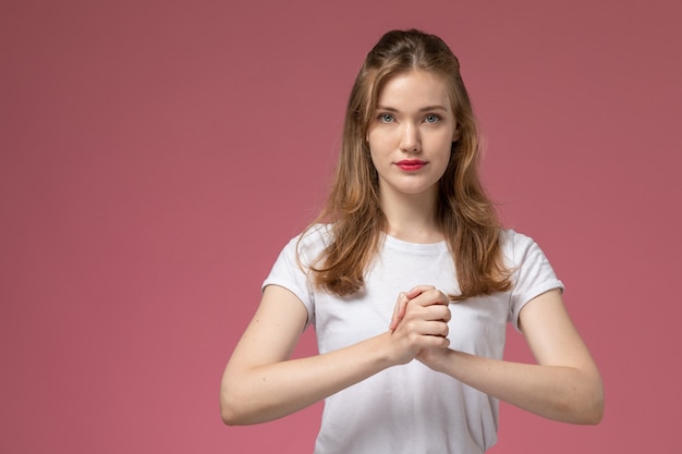 Vorderansicht junge attraktive Frau im weißen T-Shirt und in der schwarzen Hose, die auf dem Farbfoto der rosa Wandmodellfrau posieren