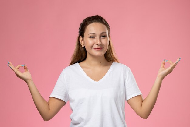 Vorderansicht junge attraktive Frau in weißem T-Shirt smi und posierend mit Meditation auf der rosa Hintergrundhaltung