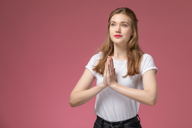 Vorderansicht junge attraktive Frau in weißer T-Shirt-Pose, die auf rosa Wandmodellfarbe weiblich jung betet