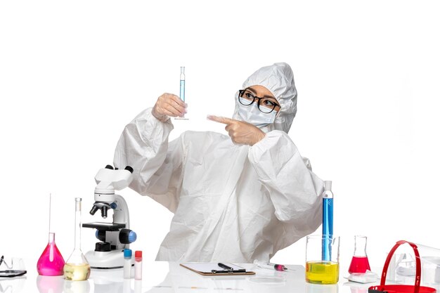 Vorderansicht junge Chemikerin im speziellen Schutzanzug, der Flasche mit blauer Lösung auf weißem Hintergrundlabor-Covid-Chemievirus hält