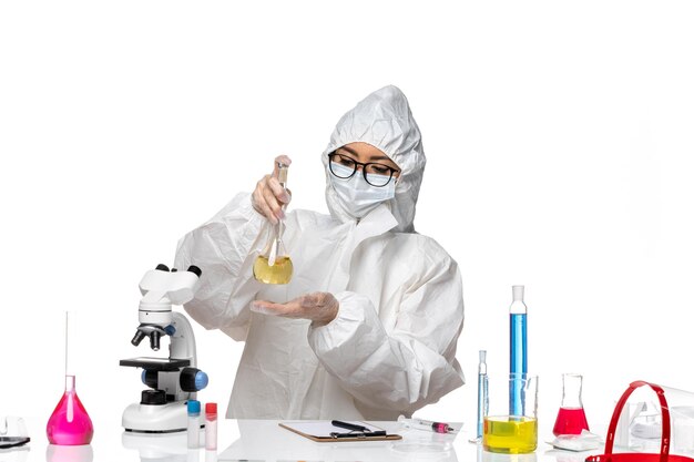 Vorderansicht junge Chemikerin in speziellem Schutzanzug, der Flasche auf weißem Hintergrundlabor covid Chemievirus hält