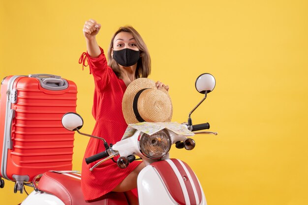 Vorderansicht junge Dame im roten Kleid auf dem Moped, das die Hand anhebt