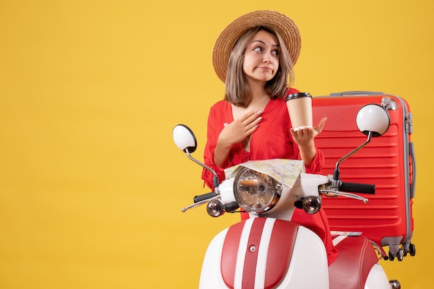 Vorderansicht junge Dame im roten Kleid mit Kaffeetasse, die Hand auf ihr Kinn in der Nähe von Moped legt