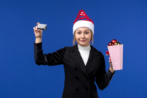 Vorderansicht junge Dame mit Baumspielzeug und Bankkarte auf blauem Wandgefühl Neujahrsfeiertag