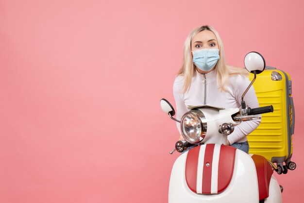 Vorderansicht junge Dame mit Maske auf Moped mit gelbem Koffer
