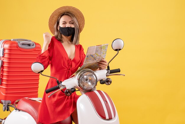 Vorderansicht junge dame mit schwarzer maske mit karte, die ihr glück in der nähe des mopeds ausdrückt