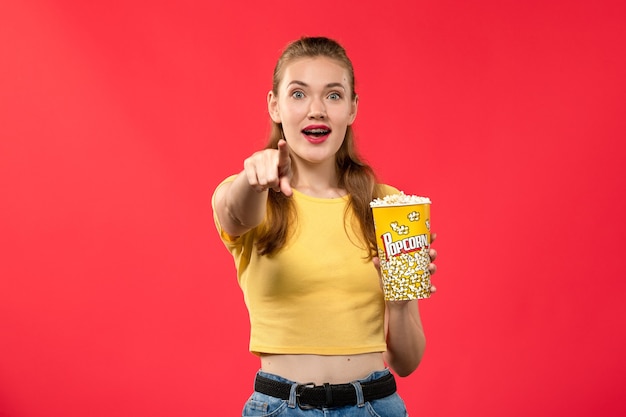 Vorderansicht junge Frau am Kino, die Popcorn auf der roten Wand des Kinokinos weiblicher Spaßzeitfilm hält