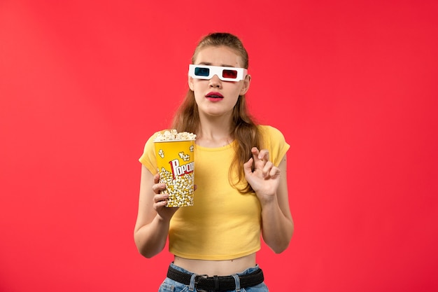 Vorderansicht junge Frau am Kino, die Popcorn in d Sonnenbrille auf der roten Wand des Kinokinos weiblicher Spaßfilm hält