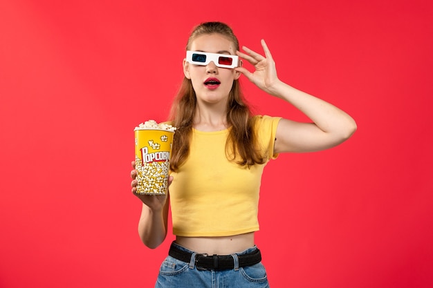 Vorderansicht junge Frau am Kino, die Popcorn-Paket in d Sonnenbrille auf der roten Wand Kino Kino weiblich Spaßfilm hält