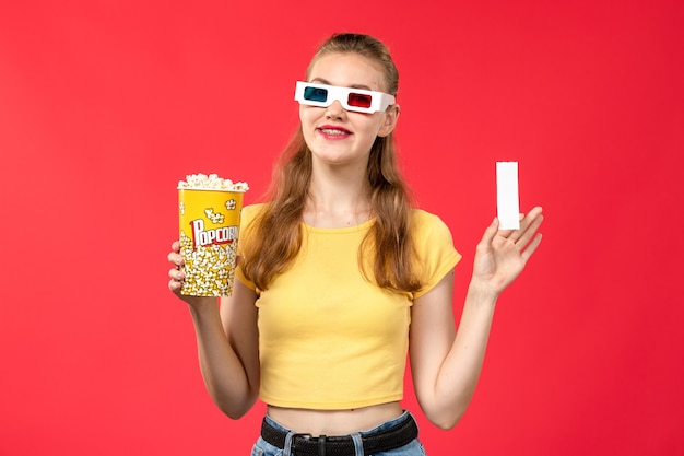 Vorderansicht junge Frau am Kino, die Popcorn-Paket und Ticket auf rotem Wandkino-Kino-Filmmädchen hält