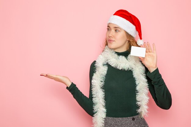 Vorderansicht junge Frau, die Bankkarte auf rosa Wandmodellfeiertag Weihnachten Neujahr Emotion hält