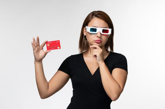 Vorderansicht junge Frau, die Bankkarte in d Sonnenbrille hält und auf weißer Oberfläche denkt