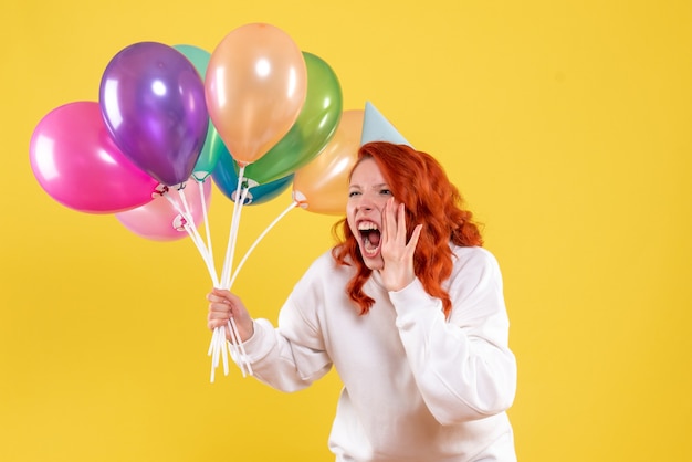 Vorderansicht junge Frau, die bunte Luftballons hält und auf Gelb schreit