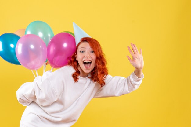 Vorderansicht junge Frau, die bunte Luftballons hinter ihrem Rücken versteckt